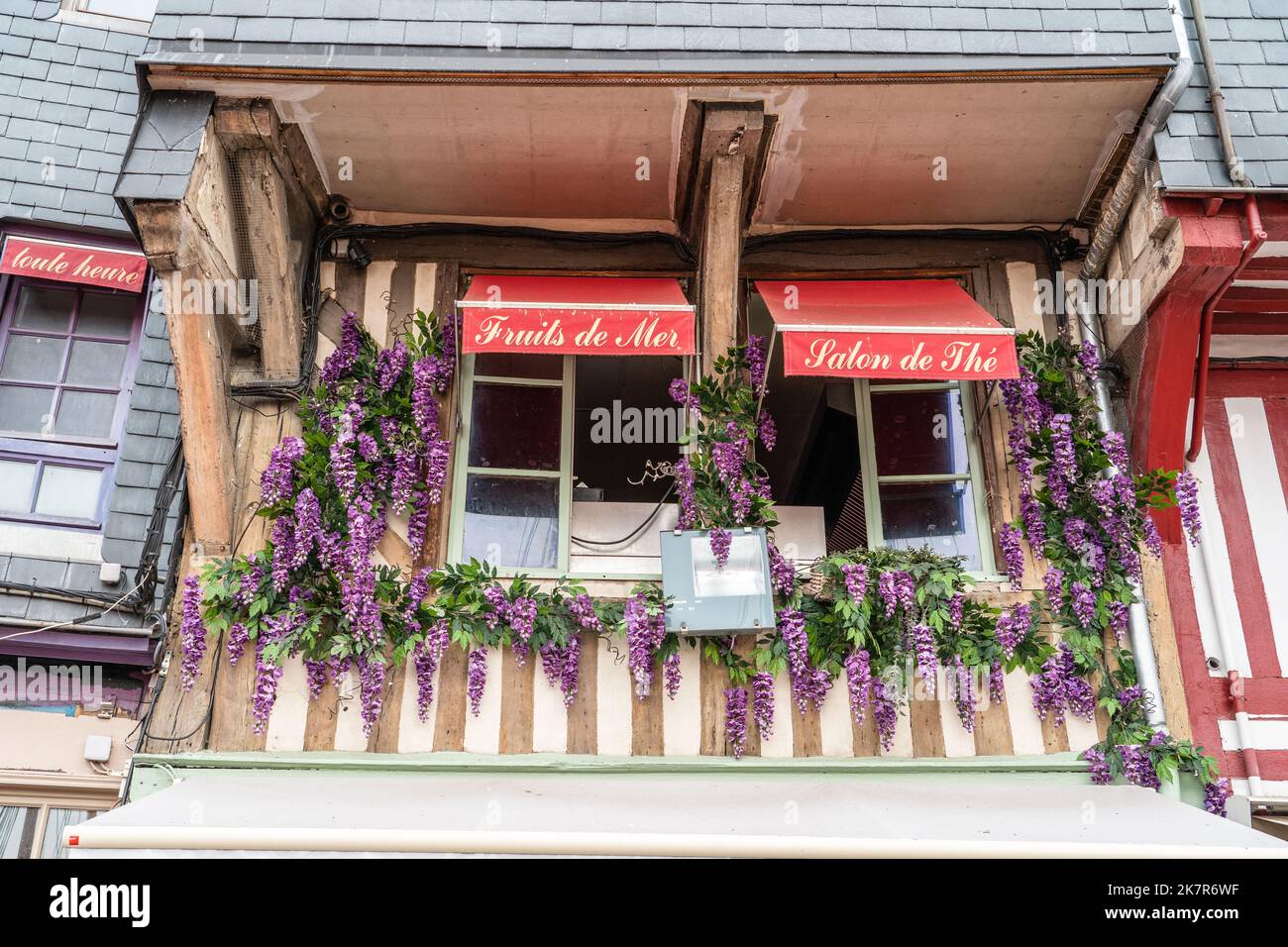 Lila Glyzinien tragen zum Charme dieses Gebäudes mit roten Markisen in Honfleur, Frankreich, bei Stockfoto