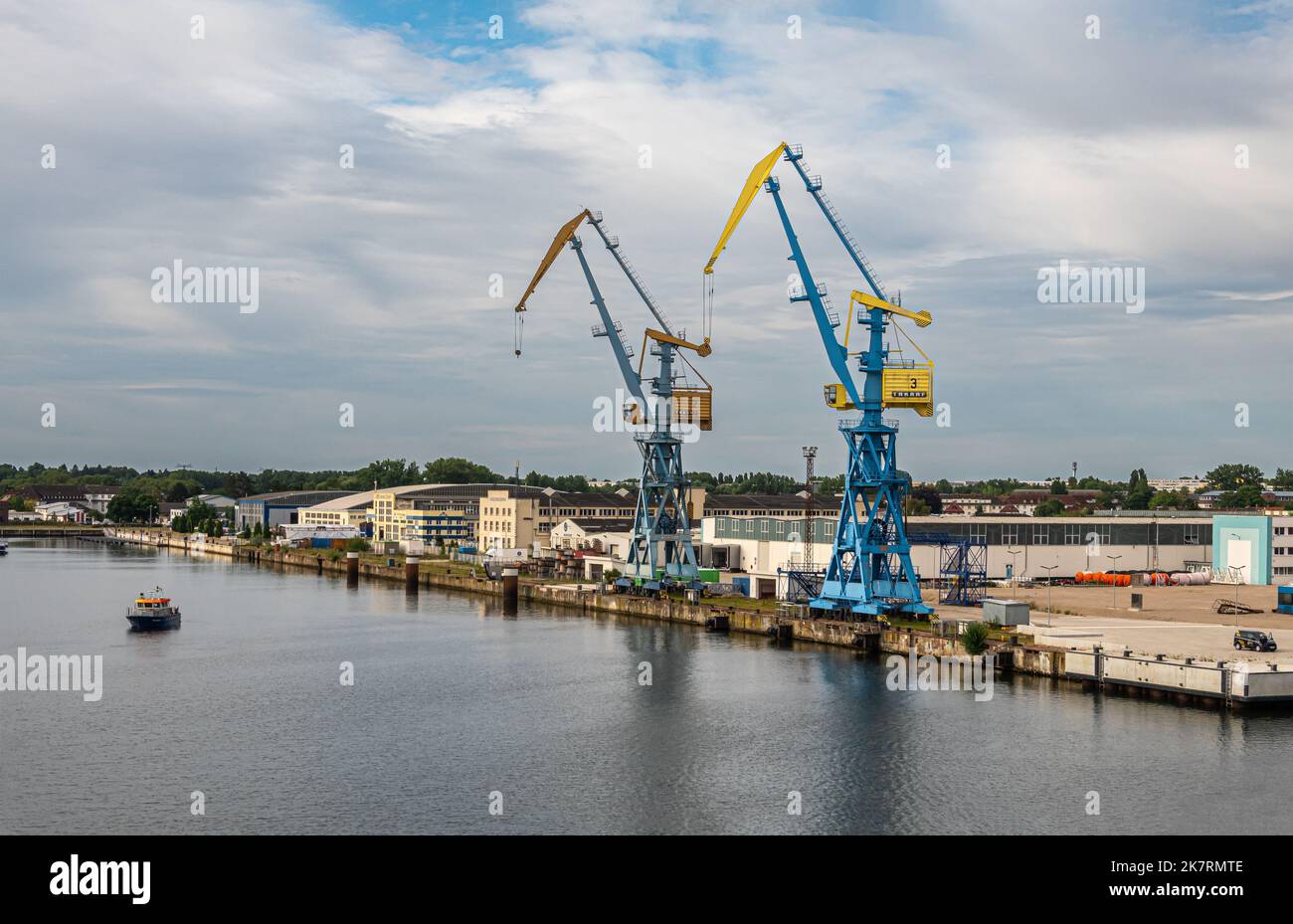 Deutschland, Wismar - 13. Juli 2022: Ostseite des Hafendocks am Westhafen mit riesigen blau-gelben Kränen am Kai. Bürogebäude und Lagerhäuser unter blauer Wolke Stockfoto