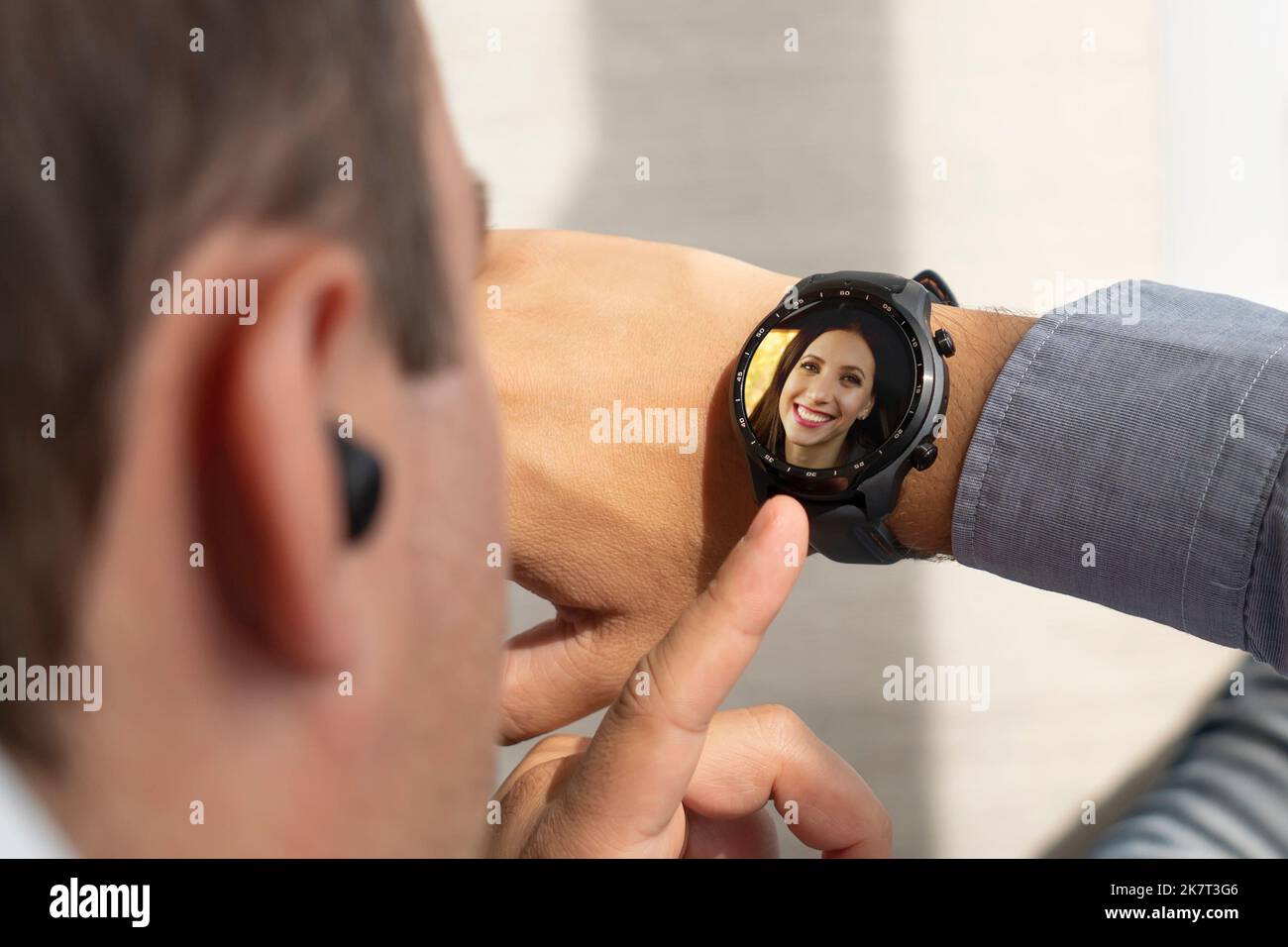 Attraktiver Mann, der auf die Uhr schaut, während er mit dem Smartphone spricht. Ankommender Anruf auf einer modernen Smart-Uhr. Der Typ drückt einen Knopf auf seiner Uhr. Stockfoto