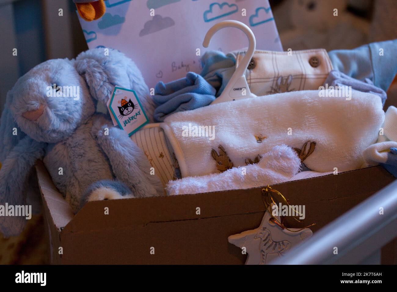 Babygeschenkkonzept und verpacktes Zubehör für neugeborene Jungen. Geschenkbox mit Decke, Kleidung, Socken, Schuhen und blauem Plüschhase. Babydusche. Stockfoto