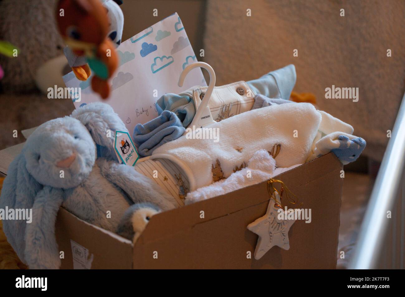Babygeschenkkonzept und verpacktes Zubehör für neugeborene Jungen. Geschenkbox mit Decke, Kleidung, Socken, Schuhen und blauem Plüschhase. Babydusche. Stockfoto