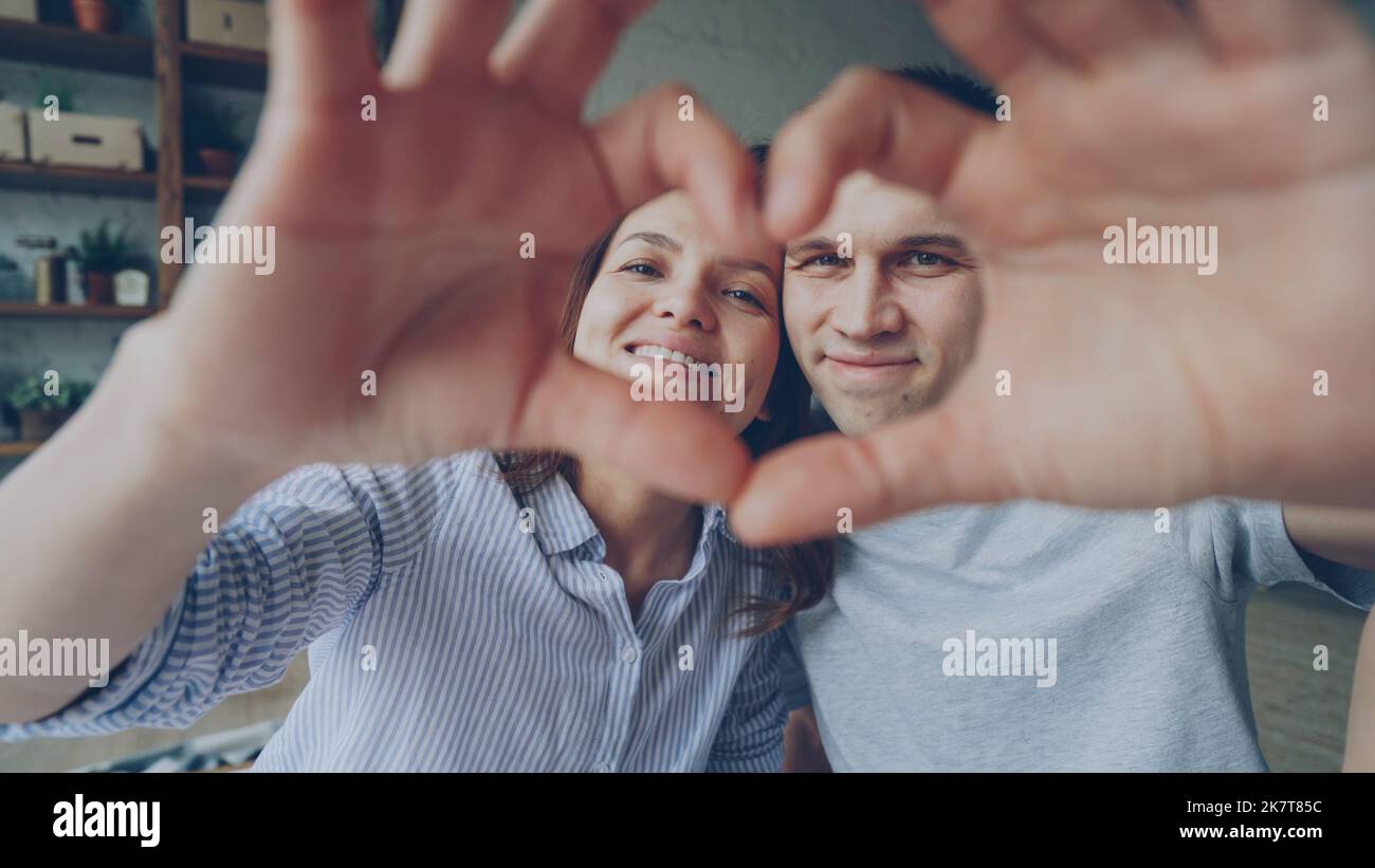 Porträt eines fröhlichen Paares, das mit den Händen Herz macht, die Kamera anschaut und lächelt. Romantische Beziehung, glückliches Eheleben und Flitterwochen-Konzept. Stockfoto