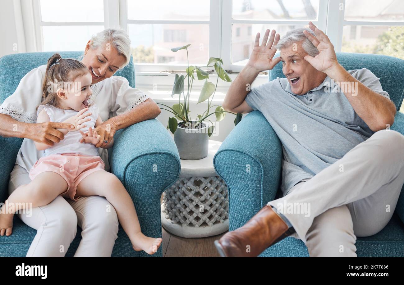 Glücklich, Großvater und Großmutter mit Kind, aufgeregt und Bonding sein dumm, komisch oder lustig im Wohnzimmer zu Hause. Älterer Mann, ältere Frau oder Stockfoto