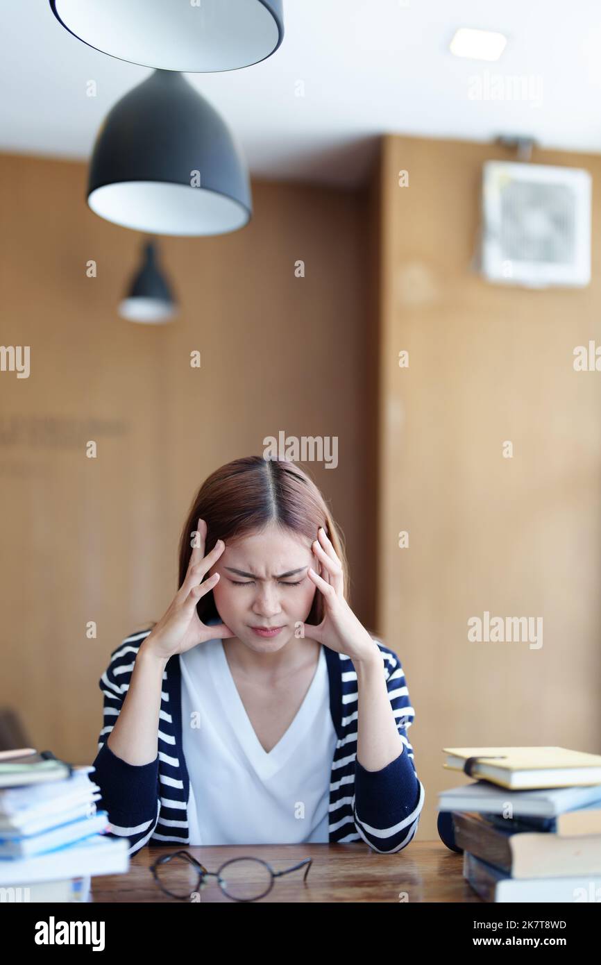 Ein Porträt eines asiatischen Teenagers, das Kopfschmerzen und Entmutigung beim Studium in der Bibliothek zeigt Stockfoto