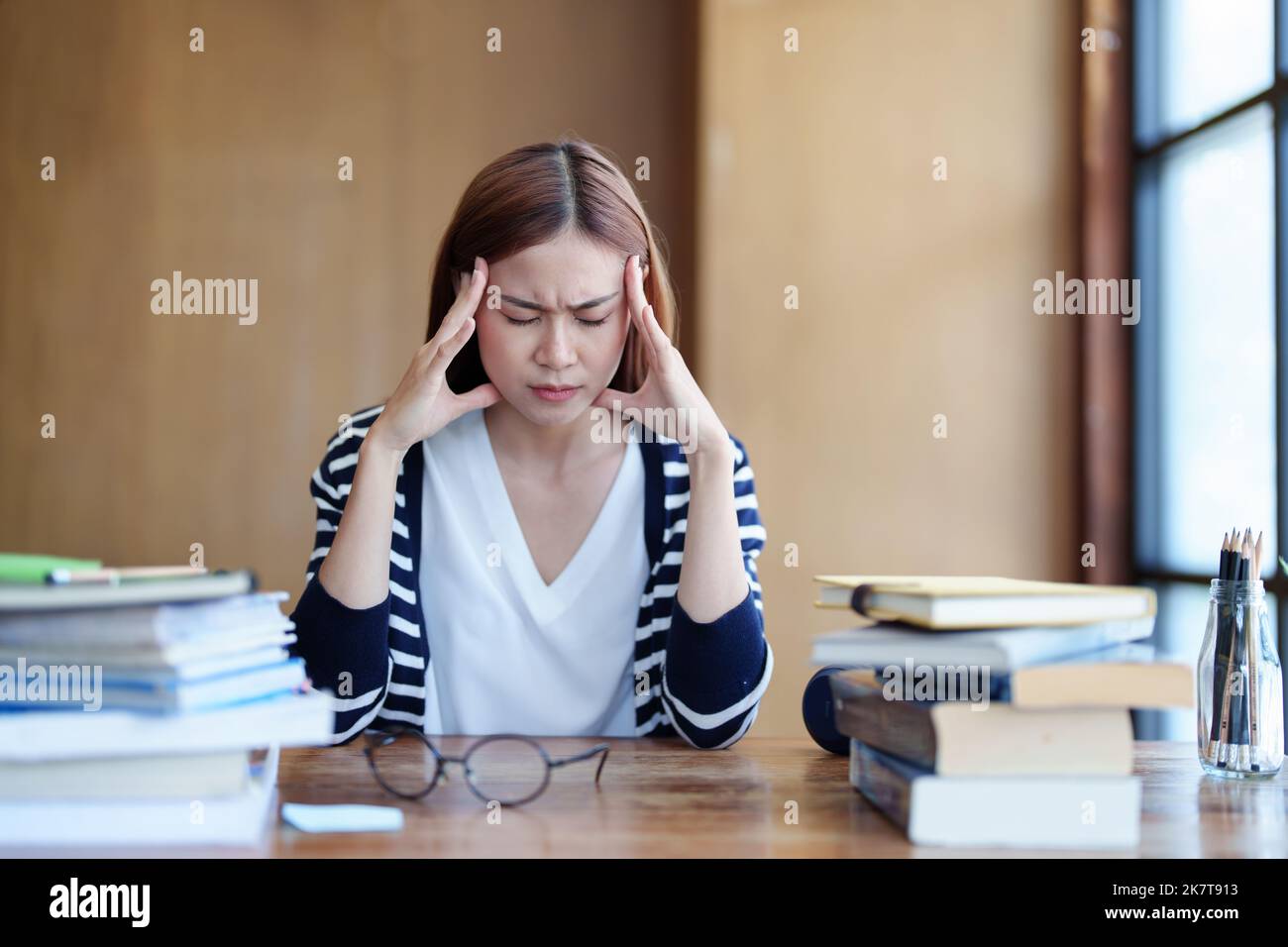 Ein Porträt eines asiatischen Teenagers, das Kopfschmerzen und Entmutigung beim Studium in der Bibliothek zeigt Stockfoto