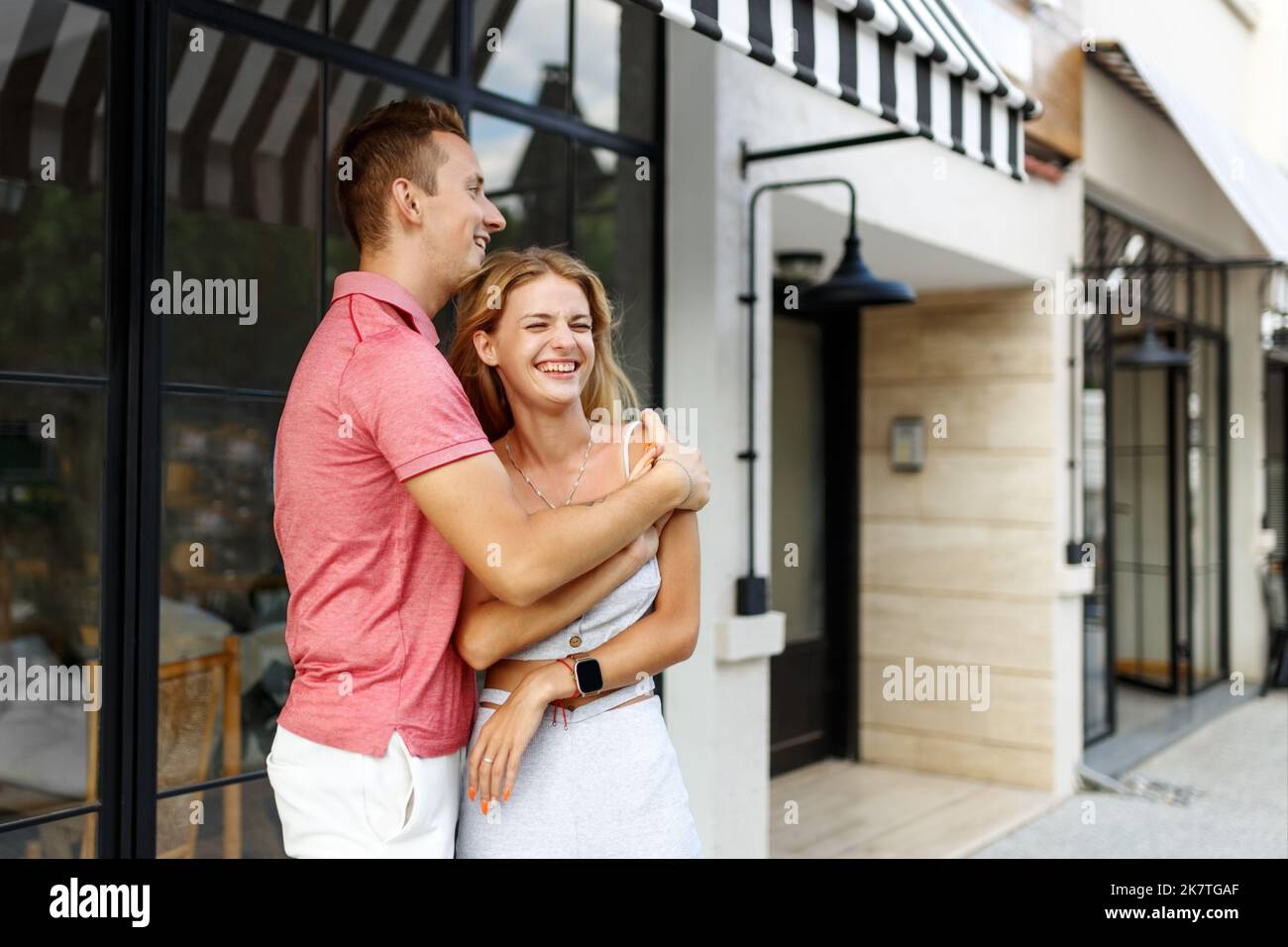 Abschiedskonzept. Erfreut glücklich lächelnde blonde Frau sagt Auf Wiedersehen oder hallo zu Freund, gibt warme Umarmung, Pose zusammen gegen Café-Platz. Wahrheitsgemäße Gefühle Stockfoto