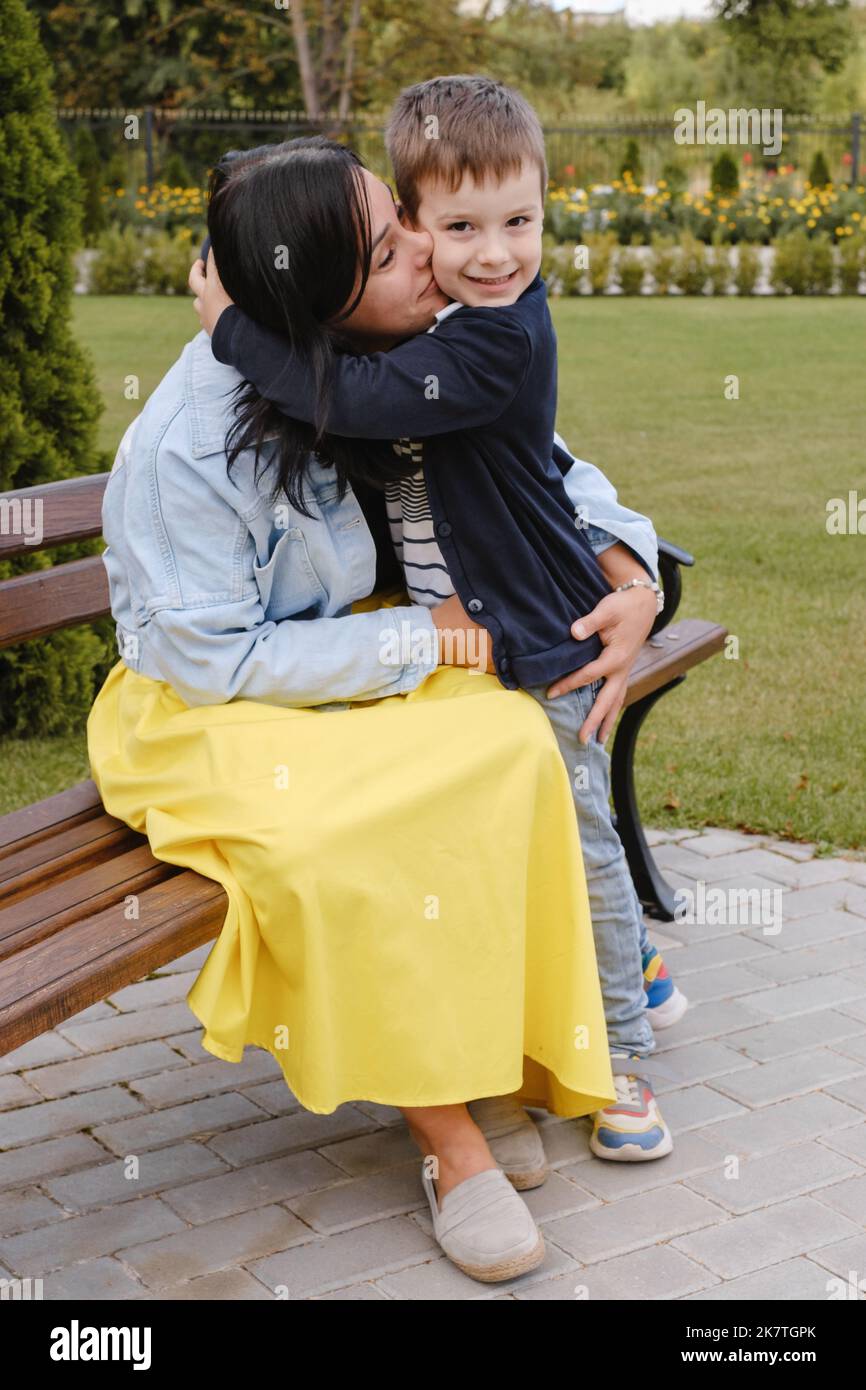 Junge umarmt Mutter im Freien auf der Bank. Mutter küsst Sohn im Park. Kostbare Momente zwischen Mutter und Sohn Stockfoto