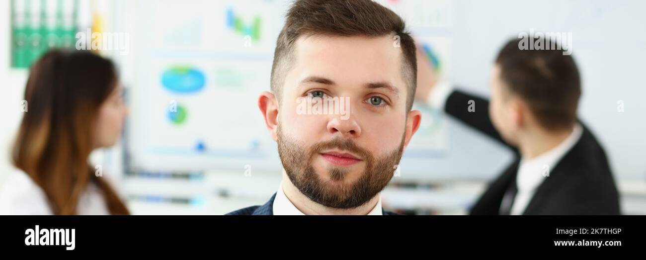 Geschäftsmann im Büro in vorzeigbarem Anzug, Kollegen im Hintergrund in der Nähe des Brettes Stockfoto