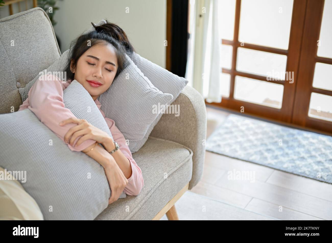Schöne junge asiatische Frau in legere Kleidung schlafen oder Nickerchen auf ihrem bequemen Sofa in ihrem Wohnzimmer. Stockfoto