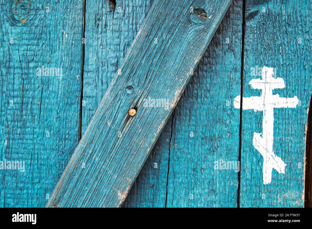 Christlich-orthodoxes Kreuz aus weißer Farbe auf alte blaue Holztür gezeichnet. Silhouetten des Kruzifix-Symbols. Christentum Religion Hintergrund. Russisch Stockfoto