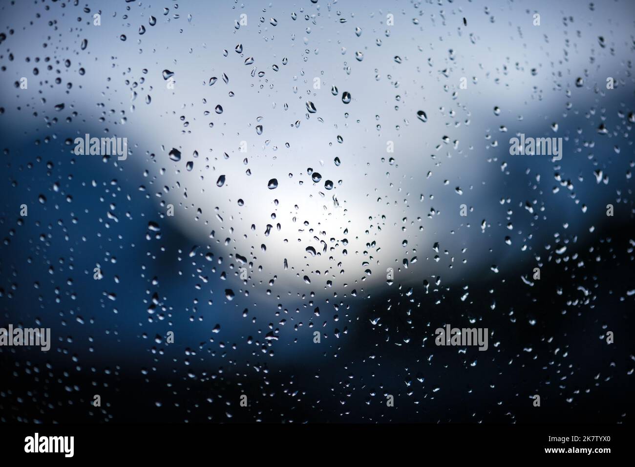 Regentropfen auf Fensterglas auf blauem Hintergrund. Selektiver Fokus. Regnerischer Stadthintergrund Stockfoto