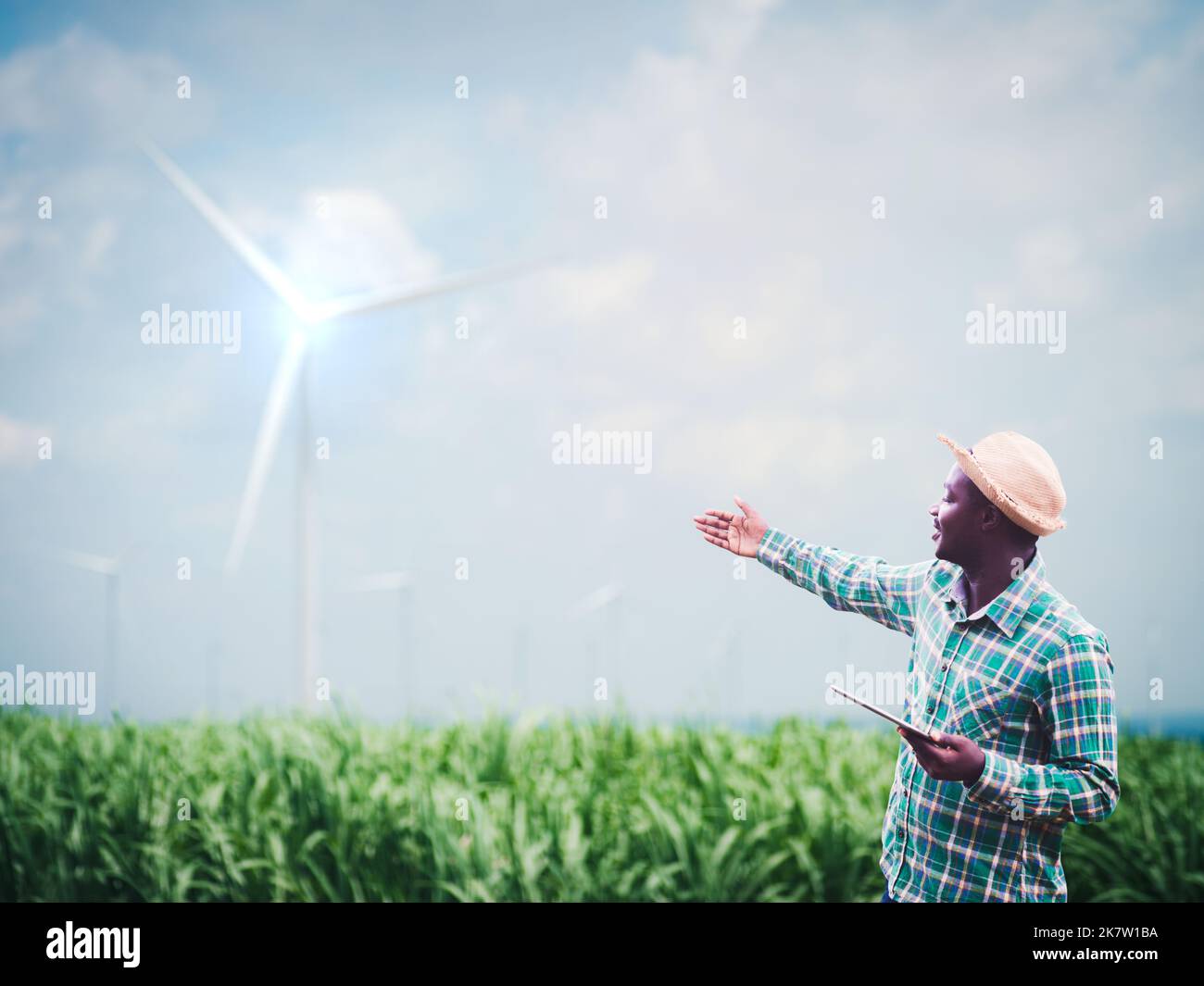 Afrikanischer Bauer steht und hält digitales Tablet auf dem Bauernhof mit Windturbine im Hintergrund.Konzept der Ökostrom Nachhaltigkeit Ressourcen Entwicklung Stockfoto