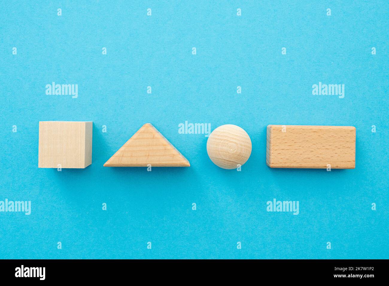 Geometrische Formen aus Holz, quadratische Figuren, Dreieck, Kugel, Rechteck mit leerer Oberfläche für Text auf blauem Hintergrund Stockfoto