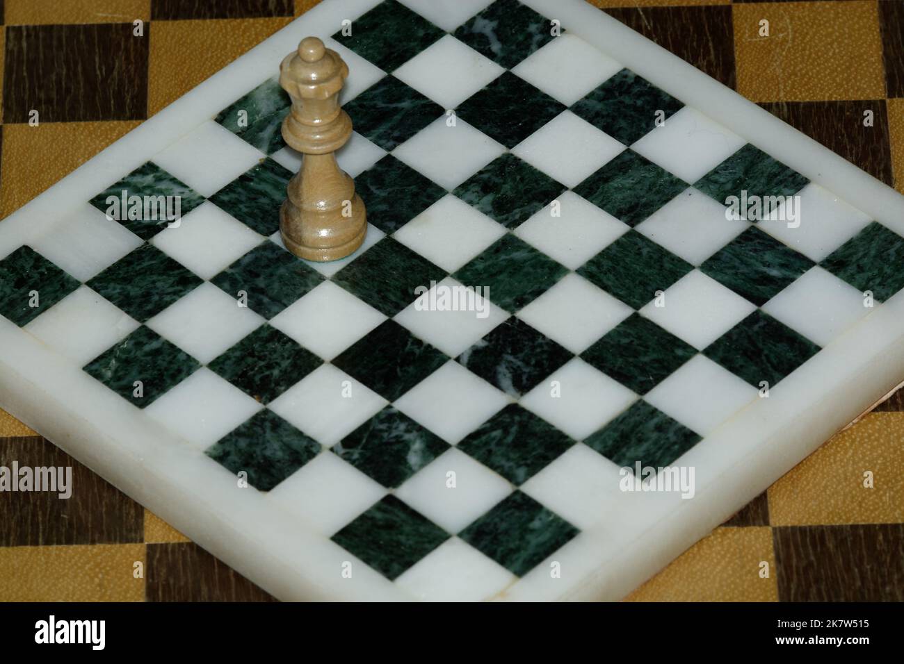 Einzelstück der Schachkönigin auf einem Quadrat in einem leeren Schachbrett, das ein Gefühl der Isolation hervorhebt. Die Königin ist zu groß für das Schachbrett - egoistisch. Stockfoto