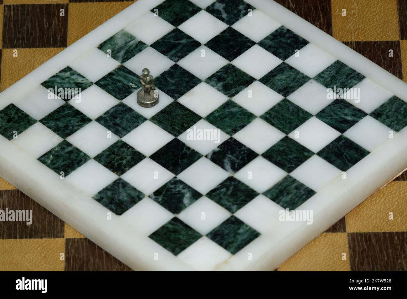 Lone Chess Pawn auf einem Quadrat in einem leeren Schachbrett, das ein Gefühl der Isolation hervorhebt. Schachbrett aus schwarzem und weißem Marmor mit Metallpfand. Stockfoto