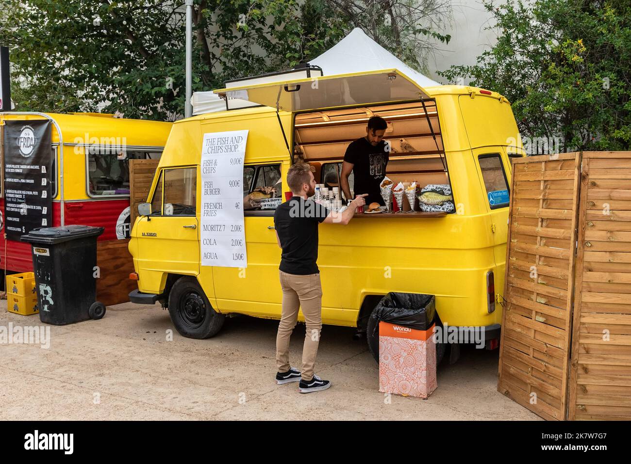 Sitges, Barcelona, Spanien - 08. Oktober 2022: Gelber Retro-Van bereit, Fast Food auf der Straße zu verkaufen, mit einem Kunden, der Chips und Fisch bestellt Stockfoto