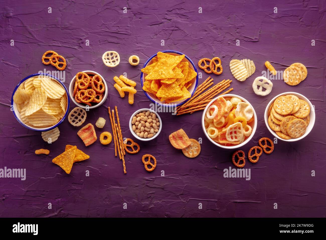 Salzige Snacks. Party Food Mix Hintergrund. Kartoffel- und Tortilla-Chips, Cracker und andere Vorspeisen in Schüsseln, darüber liegende flache Schuss Stockfoto