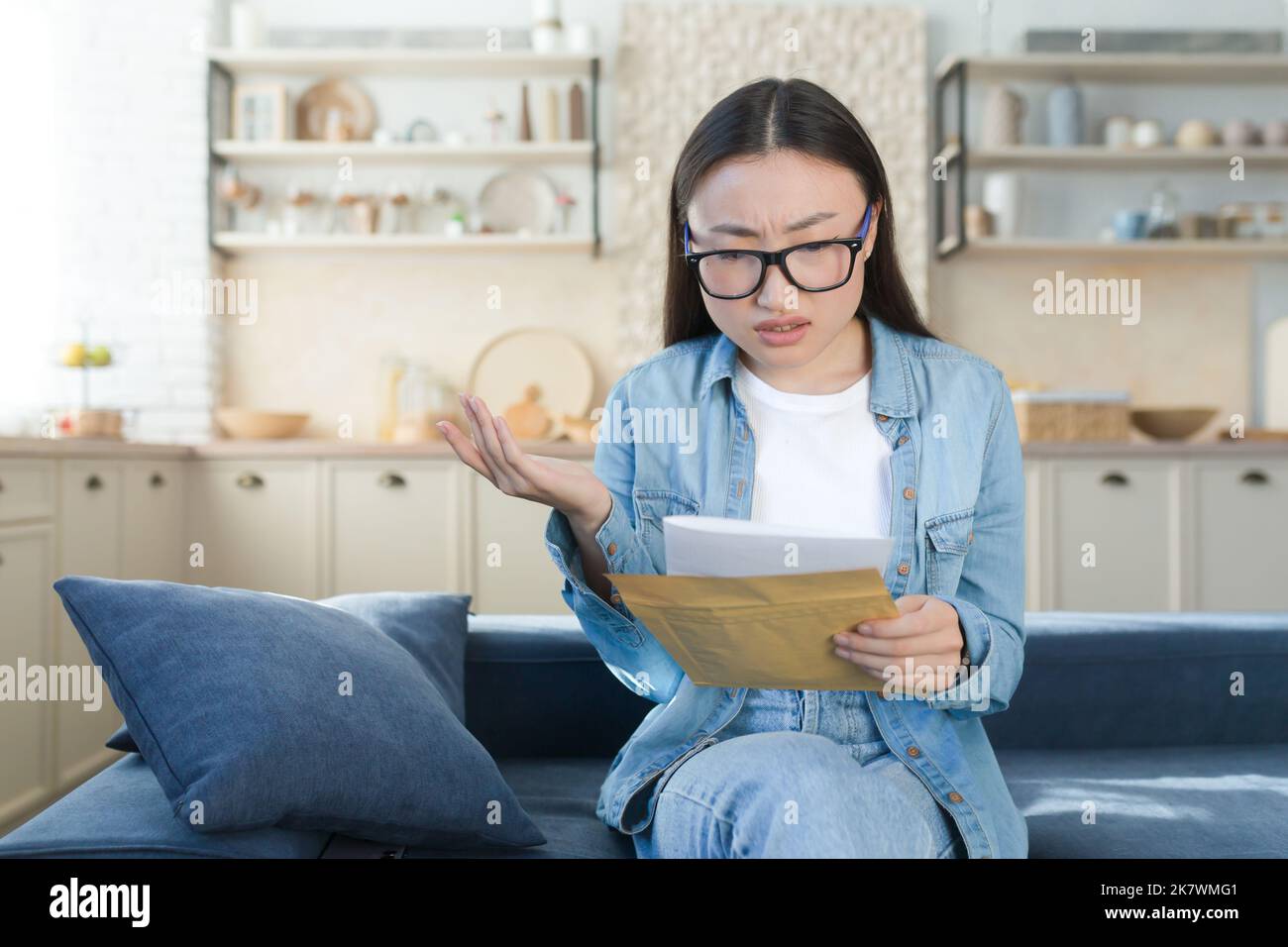 Schlechter Brief von der Bank, Frau, die zu Hause sitzt, enttäuscht und traurig, die Nachricht schlechte Nachrichten liest, asiatische Frau in der Küche. Stockfoto