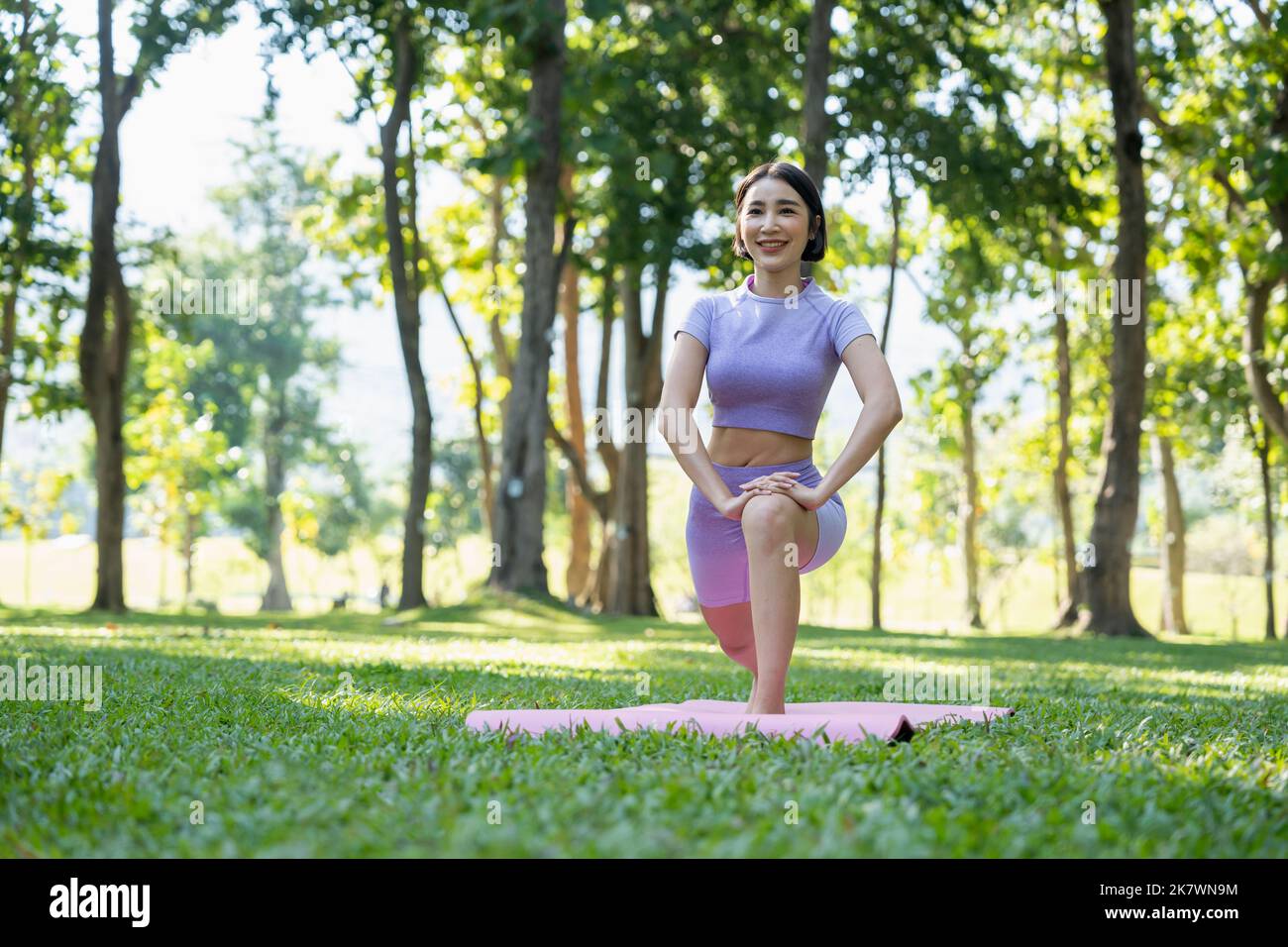 Reife, gesunde Menschen, die Yoga im Park machen. Asiatische Frau, die mit einer Yogamatte auf grünem Gras trainiert. Stockfoto