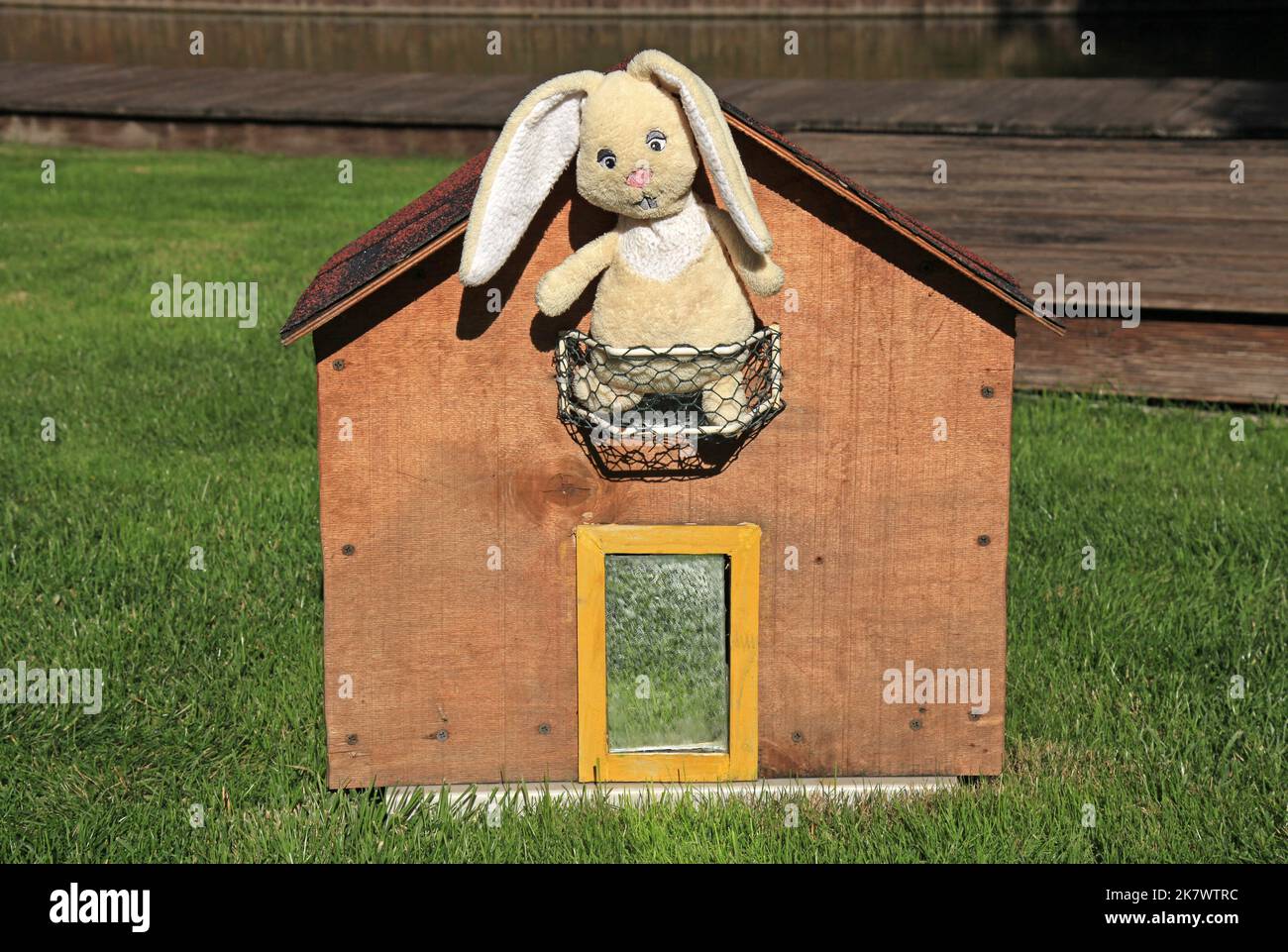 Ein Spielzeug-Kaninchen aus Plüsch sitzt auf dem Balkon eines kleinen Hauses. Kaninchen - ein Symbol von 2023 Jahr nach dem östlichen Kalender. Neujahr 2023 Stockfoto
