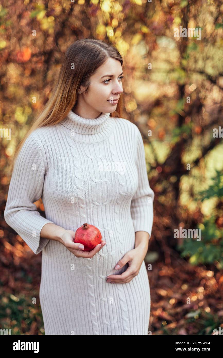 Schwangere junge Frau mit Granatapfel. Foto des fetalen Wachstums 21 Wochen Schwangerschaft. Gesunde Schwangerschaft Ernährung. Fruchtbarkeitskonzept. Platz für Text Stockfoto