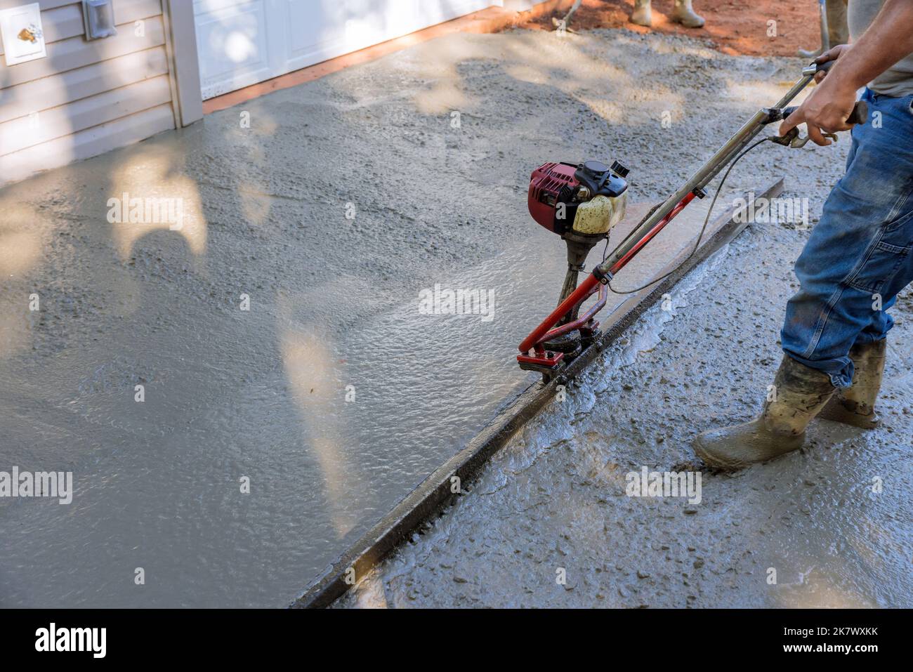 Eine Ausrichtmaschine wird verwendet, um neue, verdichtete Schicht aus Frischbeton auf neu konstruierten Einfahrten auszurichten. Stockfoto