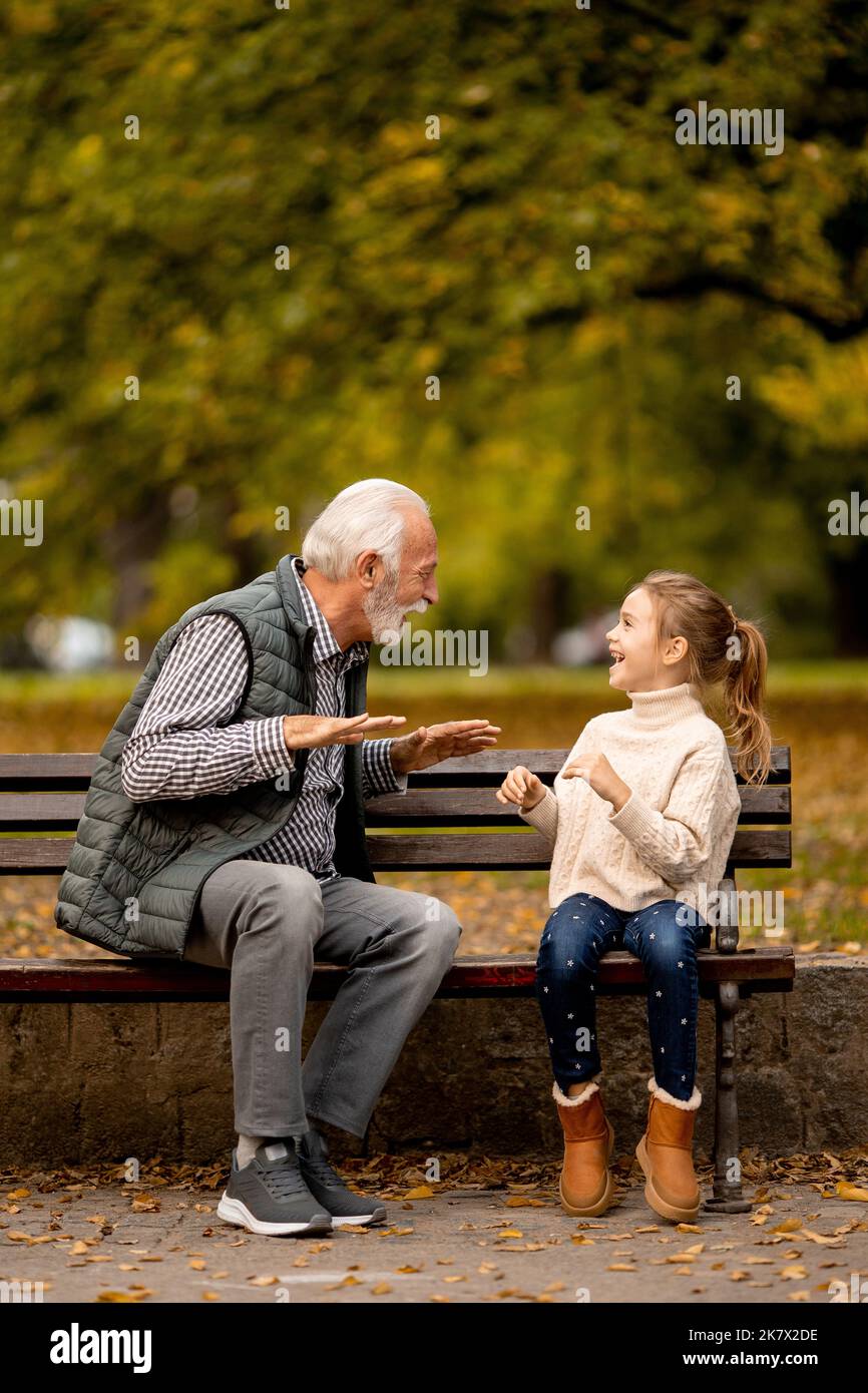 Der gutaussehende Großvater spielt am Herbsttag im Park mit seiner Enkelin ein Spiel mit roten Händen Stockfoto