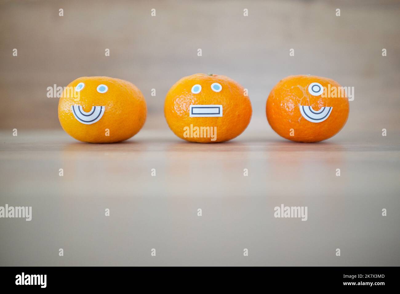 3 Mandarinen mit Mimik. Es gibt ein Smiley-Gesicht, ein stummes Gesicht und eines mit einem Smiley-Gesicht mit nur einem Auge. Stockfoto