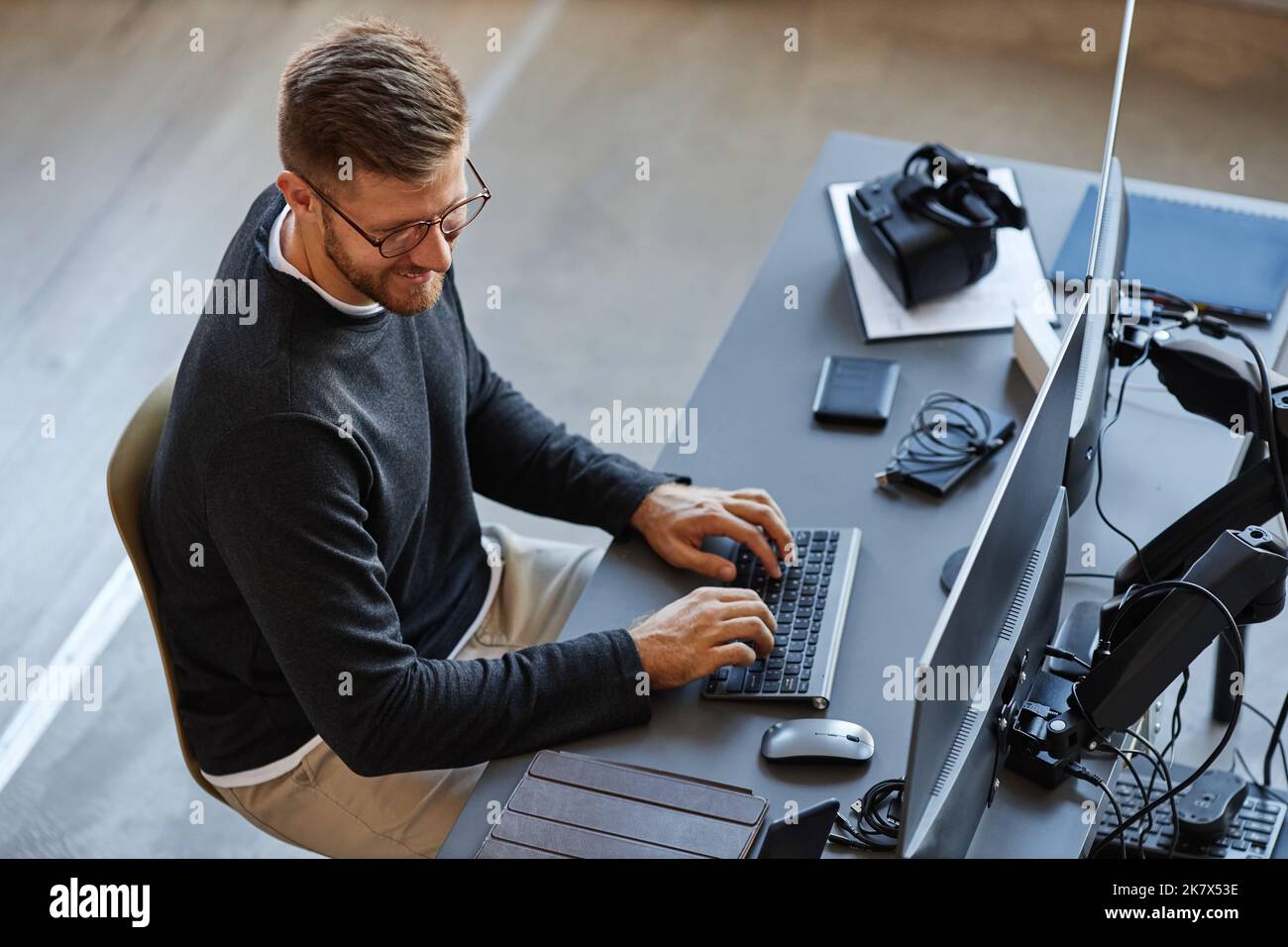 Draufsicht auf lächelnde Softwareentwickler, die Code schreiben, während sie Computer- und VR-Systeme im Büro verwenden Stockfoto