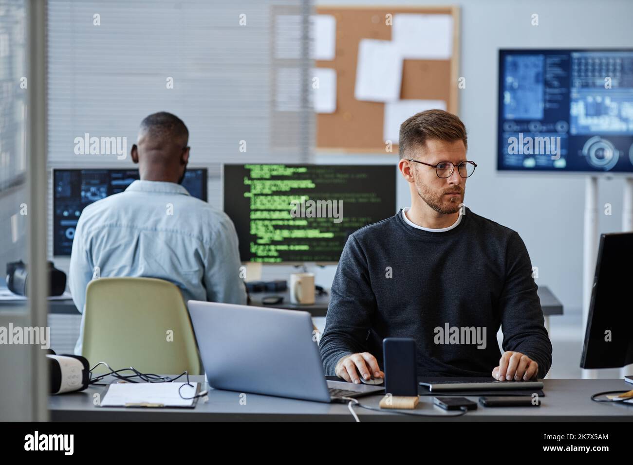 Porträt eines jungen kaukasischen Mannes, der Computer verwendet, während er Software im Büro programmiert, Raum kopiert Stockfoto