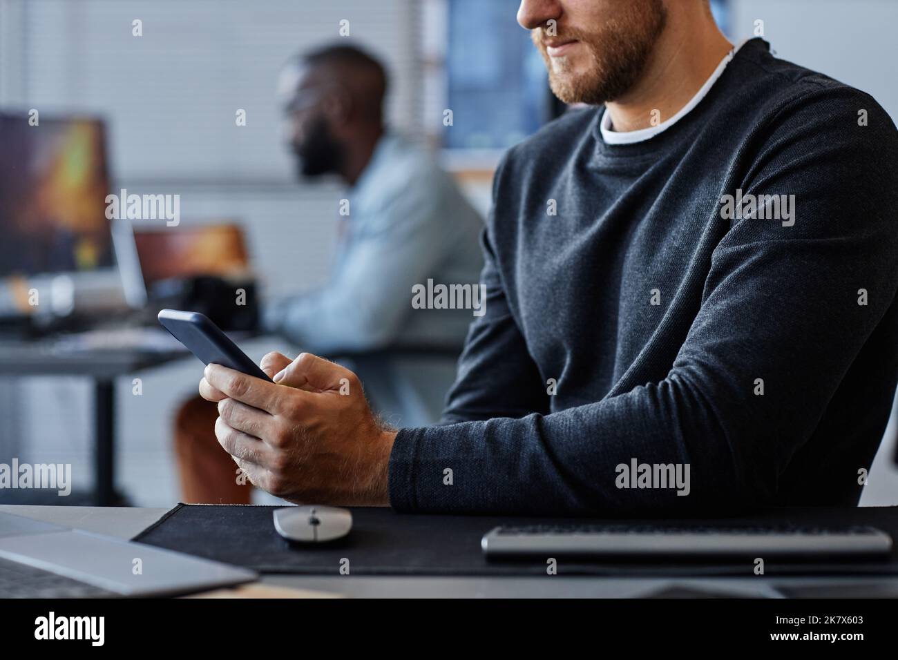 Seitenansicht Nahaufnahme eines Mannes, der am Arbeitsplatz Smartphone verwendet, während er in der Entwicklung mobiler Software arbeitet Stockfoto