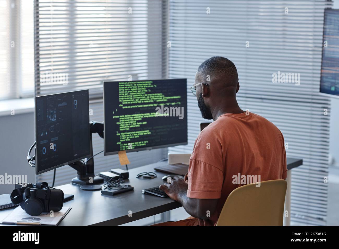 Minimale Rückansicht des afroamerikanischen Mannes, der Code in grünen Linien schreibt und Computer im Büro verwendet, Kopierraum Stockfoto