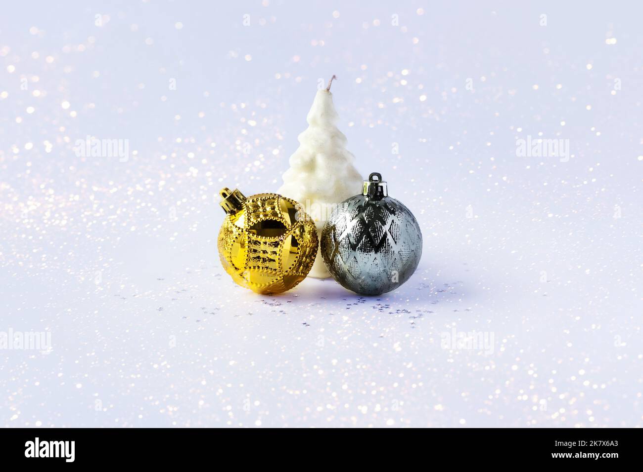 Weihnachtskomposition aus goldenen und silbernen Weihnachtskugeln und einer weißen Weihnachtsbaumkerze auf grauem Hintergrund mit Sternen Stockfoto