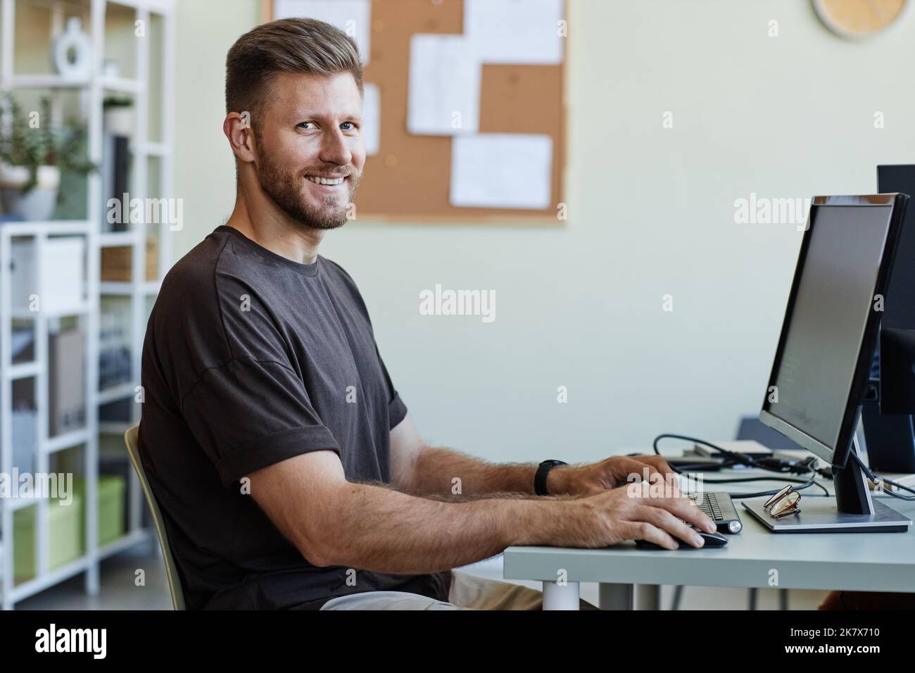 Porträt eines jungen Computerprogrammierers, der die Kamera anschaut und lächelt, während er am Arbeitsplatz im Home Office Code schreibt Stockfoto