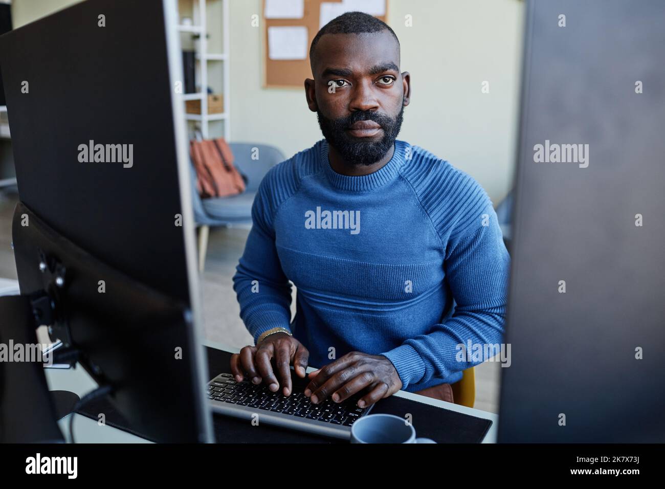 Porträt eines schwarzen Mannes, der Software am Arbeitsplatz mit mehreren Computerbildschirmen programmiert Stockfoto