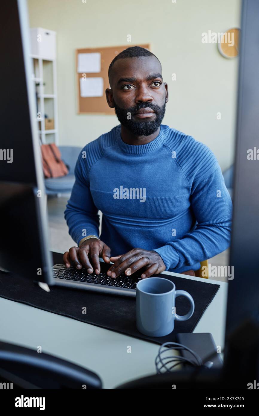 Vertikales Porträt der fokussierten schwarzen Mann Programmiersoftware am Arbeitsplatz mit mehreren Computerbildschirmen Stockfoto