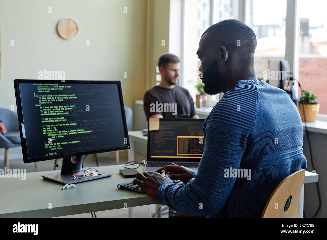 Seitenansicht Porträt eines schwarzen Software-Ingenieurs, der Code am Arbeitsplatz im Büro mit mehreren Geräten schreibt Stockfoto