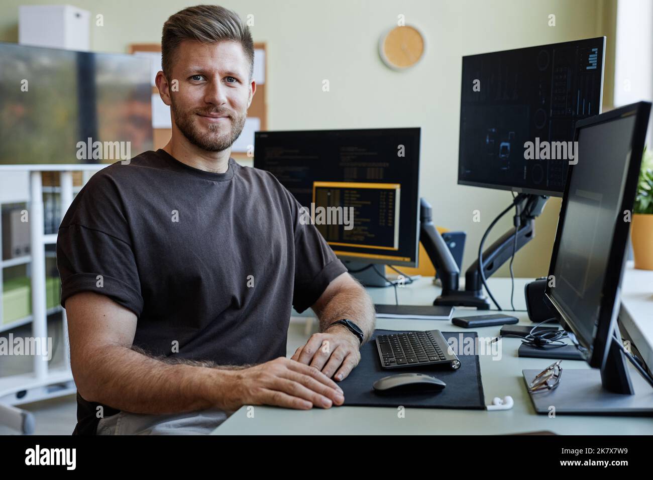 Porträt eines lächelnden Softwareentwicklers, der die Kamera anschaut, während er mit Computern am Schreibtisch sitzt Stockfoto