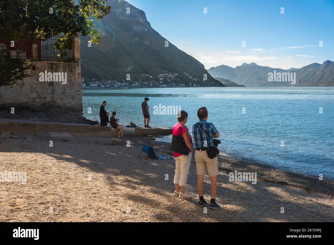 Ältere Paare reisen im Sommer von einem Paar mittleren Alters, das vom Varenna Lake Beach, Italien, aus Richtung Süden des Comer Sees blickt Stockfoto