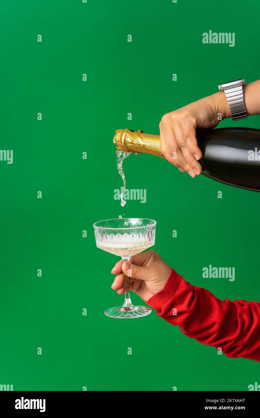 Abstrakter Hintergrund der Weihnachtsfeier, Champagner wird in einer weiblichen Hand aus einer Flasche in ein Glas gegossen. Minimalismus, grüner Hintergrund, Weihnachten a Stockfoto