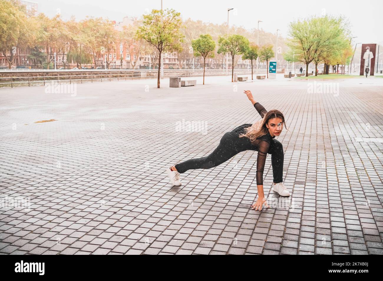 Flexible junge Frau, die im Regen auf der Straße zeitgenössischen Tanz tanzt Stockfoto