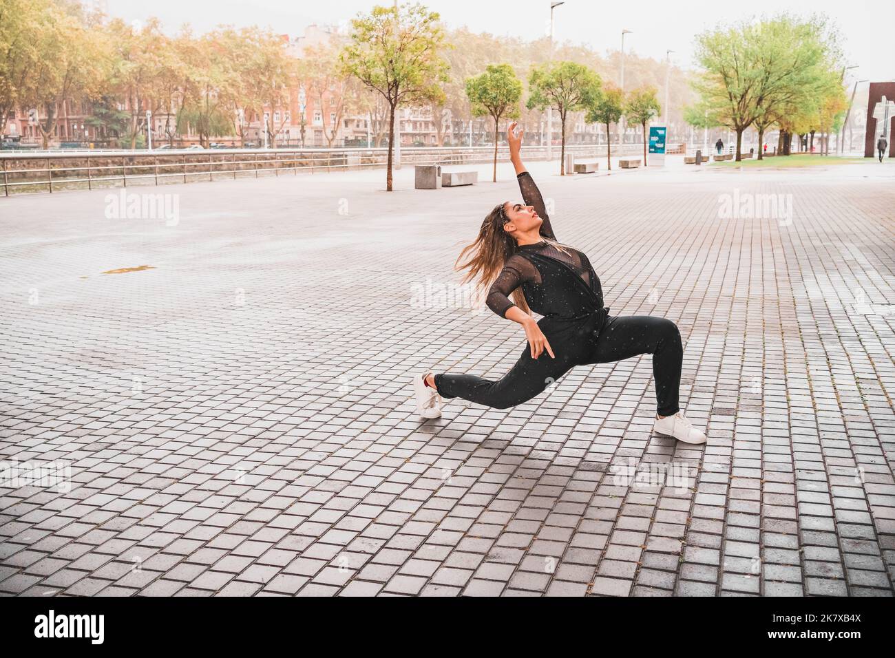 Junge Frau, die im Regen auf der Straße eine Tanzfigur zeigt Stockfoto