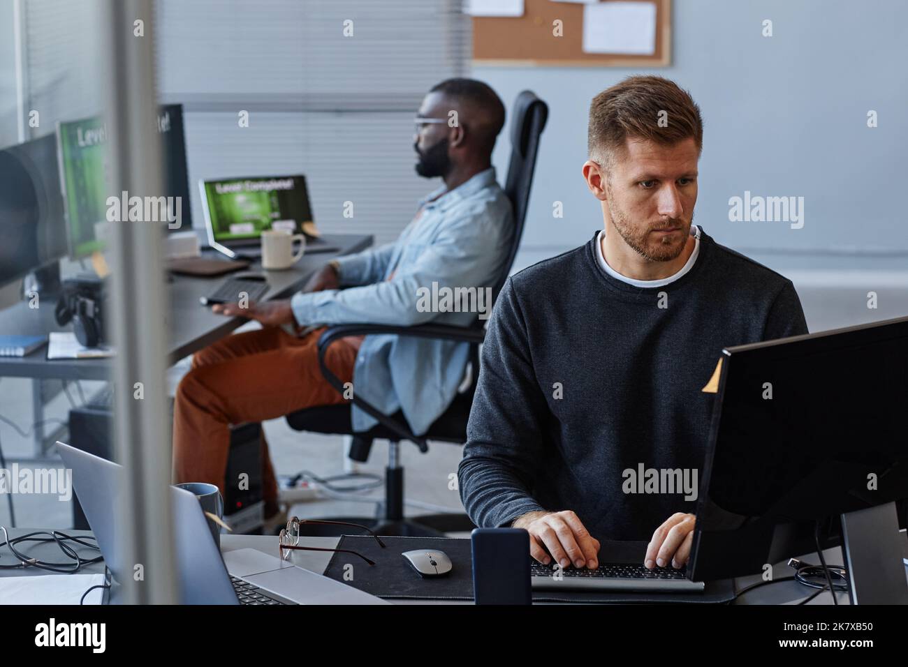 Porträt eines jungen kaukasischen Mannes, der Computer benutzt, während er mit Datenanalyse darin arbeitet, Raum kopieren Stockfoto