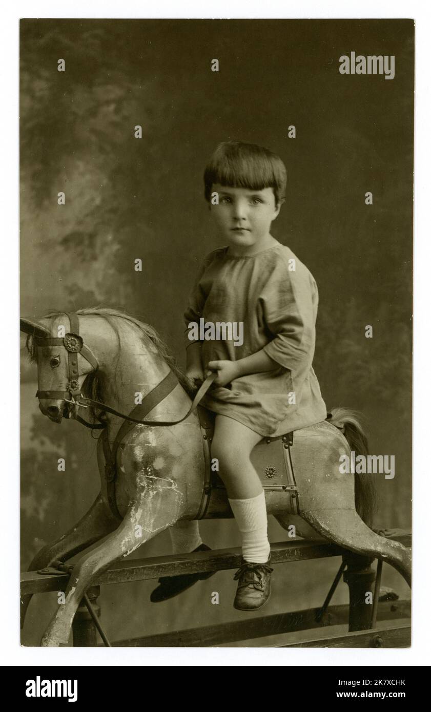 Ursprüngliche Postkarte aus der Zeit der 1920er Jahre mit einem feierlich aussehenden Kind aus den 1920er Jahren auf einem Schaukelpferd, Studio von Charles Winterbourne, Coventry, West Midlands, England, Großbritannien Stockfoto