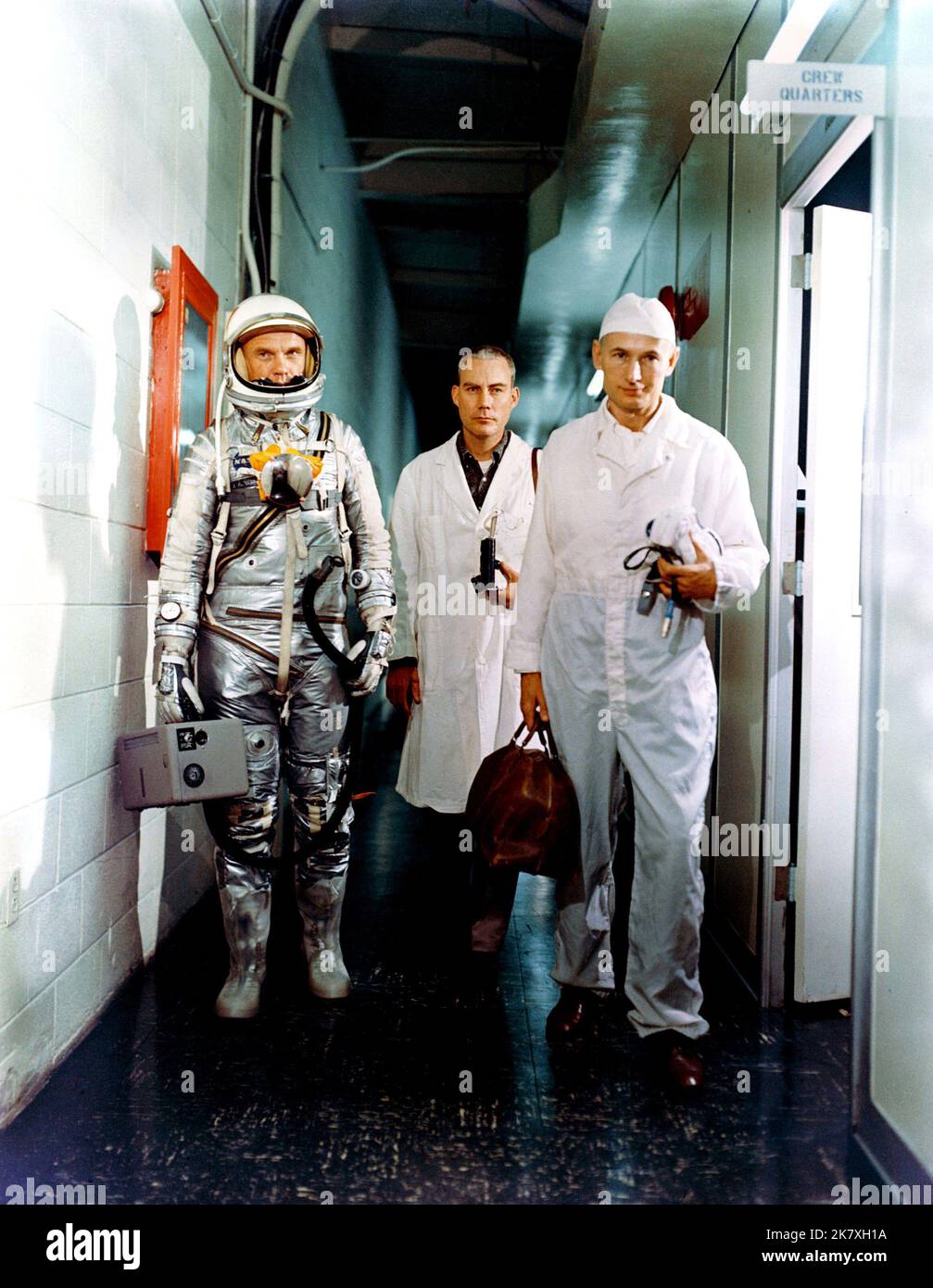 Astronaut John H. Glenn Jr. (links), Dr. William Douglas, Flugchirurg der Astronauten, und Ausrüstungsspezialist Joe Schmitt verlassen vor der Mercury-Atlas 6 (MA-6) Mission die Crew-Quartiere. Glenn ist in seinem Druckanzug und trägt die tragbare Lüftungseinheit. Stockfoto