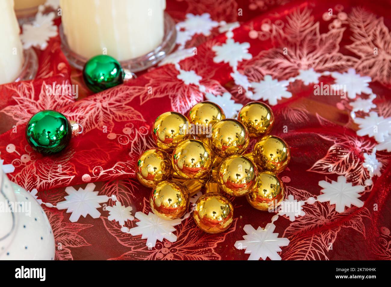 Goldene und grüne runde Weihnachtsornamente auf rotem schimmerigen Tuch mit weißer Schneeflocke Girlande auf dem Tisch Stockfoto
