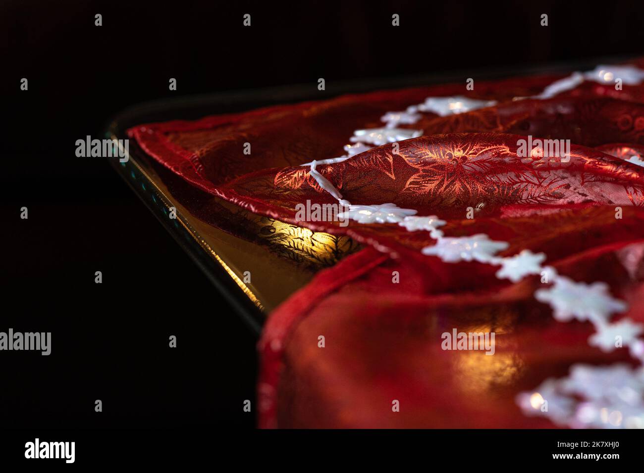 Nahaufnahme Detail der Weihnachtsdekorationen auf dem Tisch: Rotes schimmeriges Tuch und weiße Schneeflocke Girlande Stockfoto