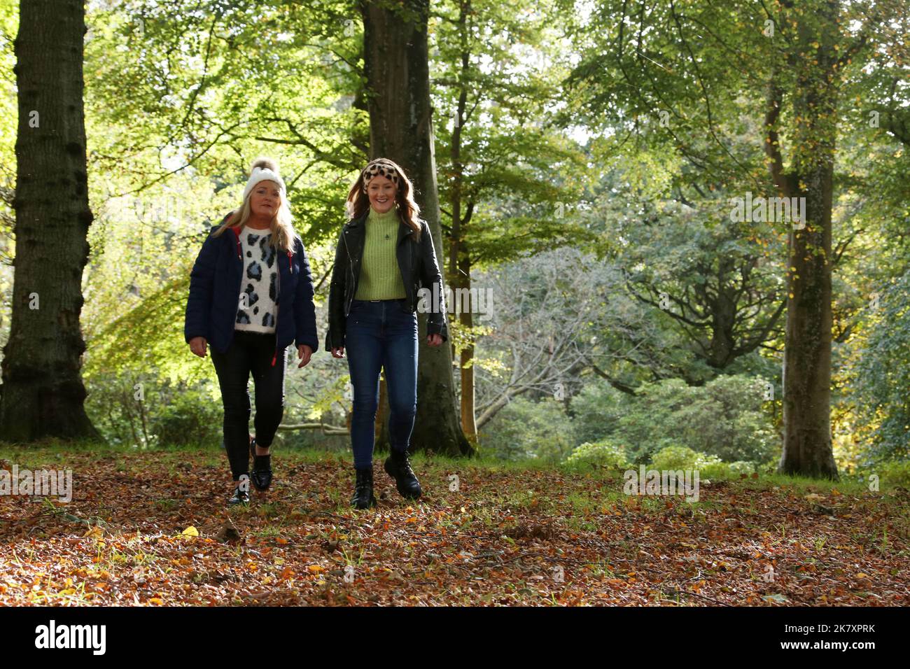 Zwei Frauen aus Kaukasien mittleren Alters in Belleisle Park, Ayr, Ayrshire, Schottland, Großbritannien, genießen die Herbstfarben, während sie in legerer Kleidung mit Wollmützen durch den Wald spazieren. Platz für Text und Kopie Stockfoto