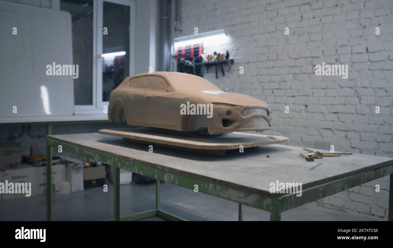 Skulptur eines umweltfreundlichen Prototypen eines Autos auf einem Holztisch in einer Werkstatt mit Werkzeugen zum Verlegen von Skulpturen. Unvollendete Skulptur eines Prototyps Modellauto. Stockfoto