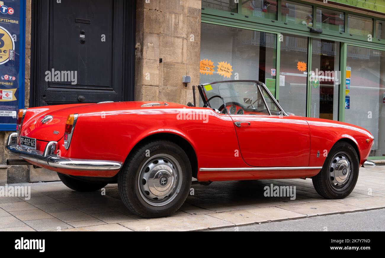 Ein klassischer Alfa Romeo 'Rosso Corsa' Spider Giula wartet auf den Eintritt zur Oldtimer- und Fahrradshow im Stadtzentrum von Sarlat-la-Caneda Stockfoto